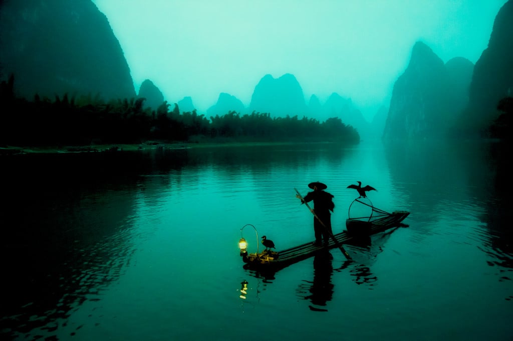 Chinese fisherman silhouette on the Li River in the early morning. To get to this spot, you need to take a boat up the Li River in complete darkness, which is a surreal experience.