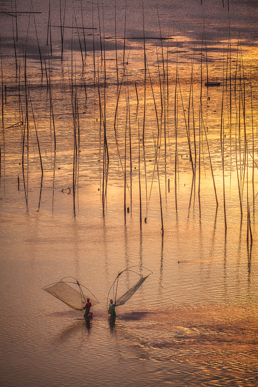 Men holding their nets during a beautiful sunrise at Bei Qi in XiaPu, China. XiaPu is famous for its mudflats that fill with water when the tide is in.