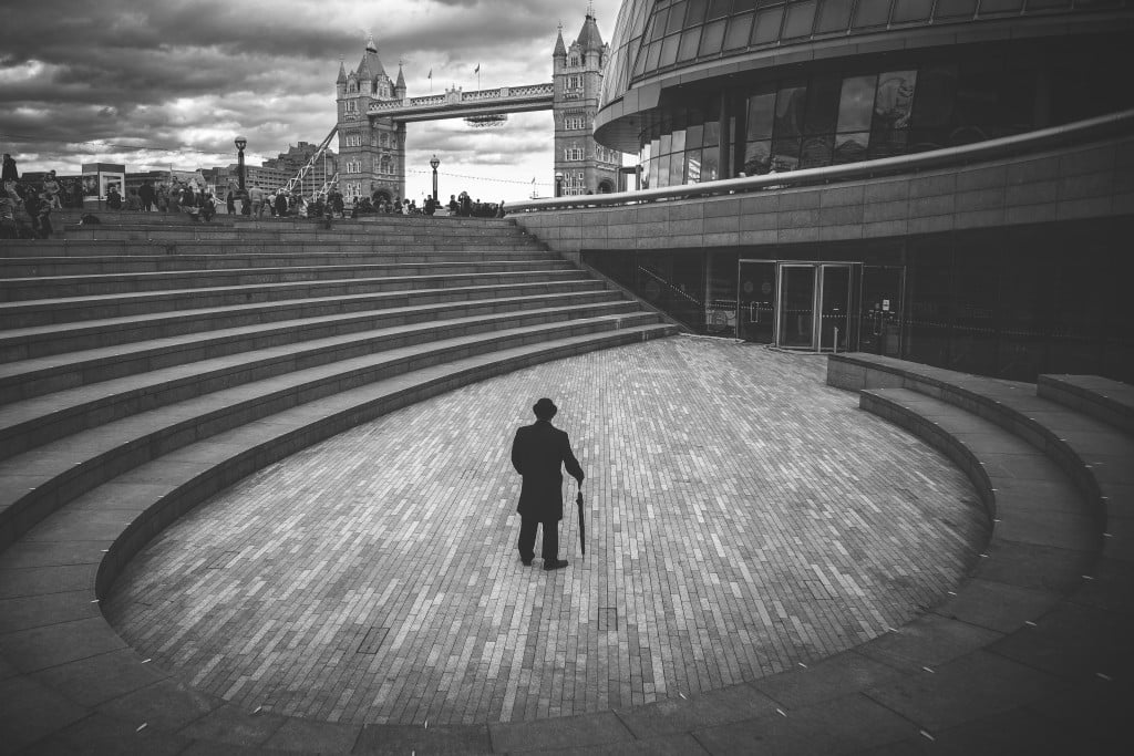 Standing tall, The Bowler Man in The Scoop looking at Tower Bridge, London. The 1,000 person sunken amphitheater, The Scoop at More London stages events all year round, from four month long More London Free Festival, through all the seasons of the year.